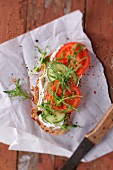 A slice of bread topped with cream cheese, cucumber, tomato and rocket