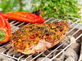 A lamb steak with a herb crust and red peppers on a barbecue