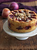 A whole gluten-free plum cake with almonds and crumbles on a round plate