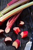 Rhubarb stalks on a wooden surface, some partially sliced
