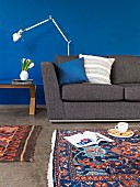 Dark grey sofa, designer standard lamp and patterned, Oriental rug in front of wall painted a rich blue