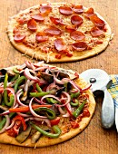 Two different pizzas with a pizza cutter on a wooden board