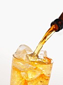 Apple cider being poured into a glass with ice cubes