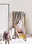 Sleeping area with feminine ambiance - hand-made wardrobe with curtained front next to partially visible four-poster bed