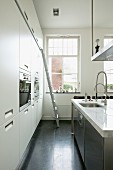 Kücheninsel mit Marmor-Arbeitsplatte in weisser Einbauküche mit schwarzen Bodenfliesen