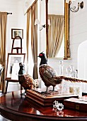 Stuffed pheasants on table between antique boxes, gilt-framed mirrors and elegant easel
