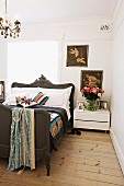 Französisches Bett mit antikem, geschnitztem Holzrahmen neben modernem Nachtkästchen in Schlafzimmer mit naturbelassenem Dielenboden