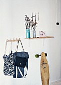 Still-life cloakroom arrangement with ceramic vases on wall-mounted shelf, collection of bags on hooks and vintage skateboard