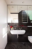 White sink on wall with black mosaic tiles below mirrored cabinets