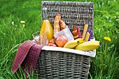 A picnic basket filled with fruit, rolls and orange juice