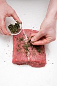 Herbs being strewn onto a slice of raw beef