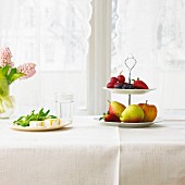 Feldsalat mit gebackenem Ziegenkäse neben Etagere mit frischem Obst auf Tisch mit weisser Tischdecke