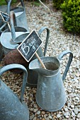 Old zinc jugs with price labels on a gravel path