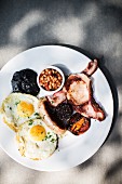 An English breakfast with fried eggs, sausage, bacon, black pudding, baked beans and fried tomatoes