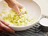 Grated white cabbage being mixed with salt