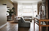 Interior in warm shades of grey and wood with sofa combination in front of bay window; display cabinet in foreground