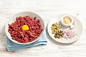 Ingredients for a hamburger: minced meat with egg yolk, onions, cornichons, capers and mustard