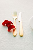 Golden cutlery and red rose petals