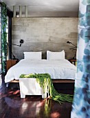 Doppelbett mit schwarzen Gelenkleuchten vor Sichtbetonscheibe; Kleiderbank mit Kunstobjekt aus grünen Filzkordeln