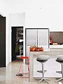 Detail of modern kitchen with side-by-side fridge freezer and stools at concrete breakfast bar; view into pantry through open door to one side