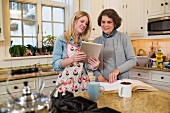 Ältere Frau und Enkelin überprüfen Rezept auf PC-Tablet in der Küche