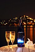Nighttime atmosphere with two glasses and bottle of sparkling wine on table by the sea