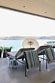 Sun loungers and small parasol on roofed terrace with glass balustrade and sea view