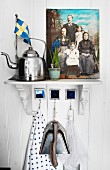 Vintage kettle next to painted family portrait on bracket on white wooden wall