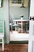 Blick durch offene Tür auf Essplatz mit einfachen Holzstühlen und Retroleuchte in der Küche eines alten, schwedischen Holzhauses
