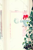 Doll wearing red bobble hat on swing next to houseplant in front of window