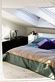 Double bed with blanket and scatter cushions below skylights in vintage attic bedroom