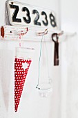 Festive bag for sweets made from red, polka-dot fabric hanging from shabby-chic wall hooks below number plate