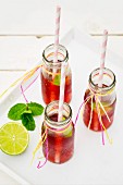 Three small bottles of iced tea with lime and peppermint on a white tray