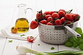 Tomaten im Küchensieb, daneben Basilikum, Zwiebel und Olivenöl