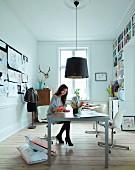 Woman at table below pendant lamp with black lampshade in study with fitted bookcase