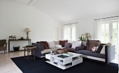 Modern, white coffee table with apertures in front of corner sofa on dark blue rug in spacious living room