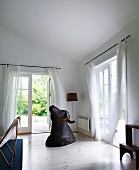 Buffalo hunting trophy on wooden floor in corner of living room with airy, white curtains on French windows