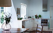 Modern, L-shaped kitchen counter with glass vase on wooden table in foreground