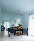 Chairs upholstered in blue around wooden table in open-plan interior with minimalist atmosphere