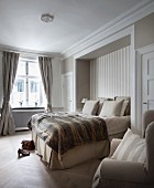 Bedspread and stacked pillows on box-spring bed in niche in traditional bedroom with subdued colour scheme