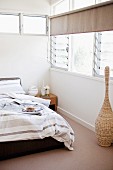 Bett mit gestreifter Bettwäsche in graubraunen Tönen in Schlafzimmerecke mit Fenster