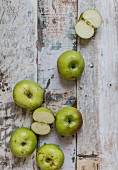 Green cooking apples, whole and halved, on a weathered wooden surface