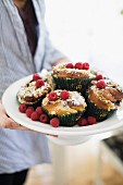 Person holding dish of muffins and fresh raspberries