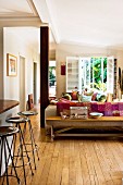 Low wooden table against back of sofa, bar stools and counter to one side in rustic interior