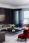 Roter Sessel vor massgefertigtem, filigranem Coffeetable in elegantem Wohnzimmer, dunkler, transparenter Vorhang an Balkontür