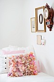 Scatter cushion with pink ruffles on couch below antique clock and various framed picture on wall