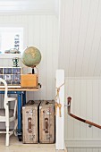 White, wood-clad, open-plan attic room with desk and vintage suitcases next to balustrade at head of staircase