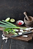 Sliced spring onions on a chopping board with a mortar, chillis and limes in the background