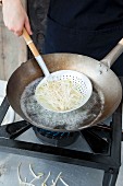 Cooked oriental noodles being removed from a wok with a draining spoon