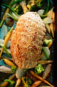 A whole roast pork roulade on a bed of vegetables in a roasting tin